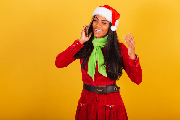 Beautiful black Brazilian woman dressed in christmas clothes, santa claus, smartphone and voice call - Fotoğraf, Görsel