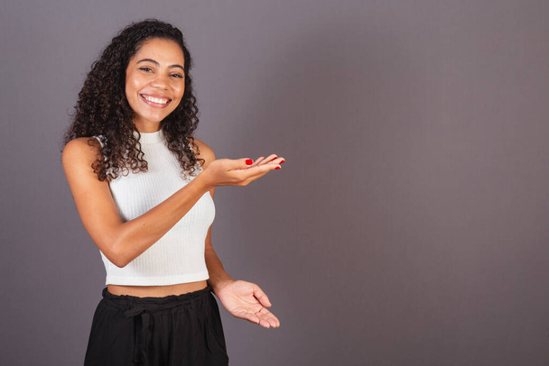 Young Brazilian black woman presenting with her hands to the right, publicity photo. - Φωτογραφία, εικόνα