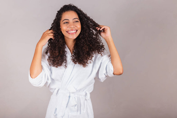 Brazilian black woman, wearing bathrobe and towel. curly hair, spa, beauty center, hair care. showing hair. curls. - Foto, Imagen