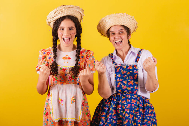 grandmother and granddaughter dressed in typical Festa Junina clothes. Calling with the hands, inviting, come here. - Foto, imagen
