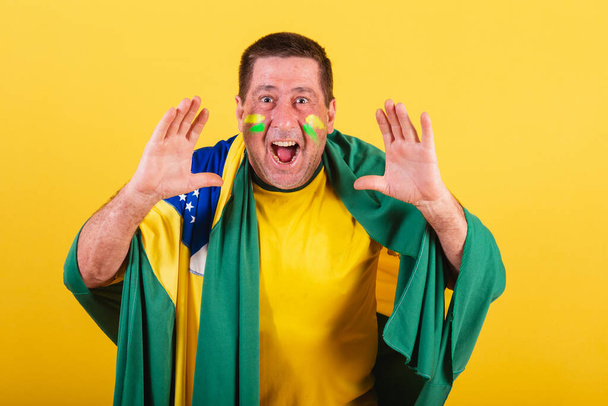 Взрослый мужчина, футбольный фанат из Бразилии, использует флаг, кричит о повышении. рекламное фото. - Фото, изображение