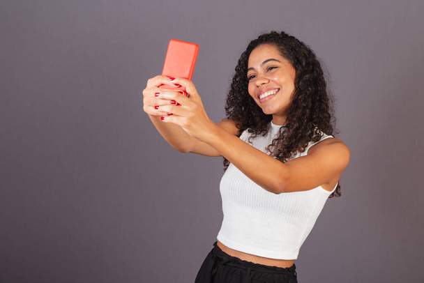 Young Brazilian black woman taking selfie, self portrait with red cellphone. - Zdjęcie, obraz