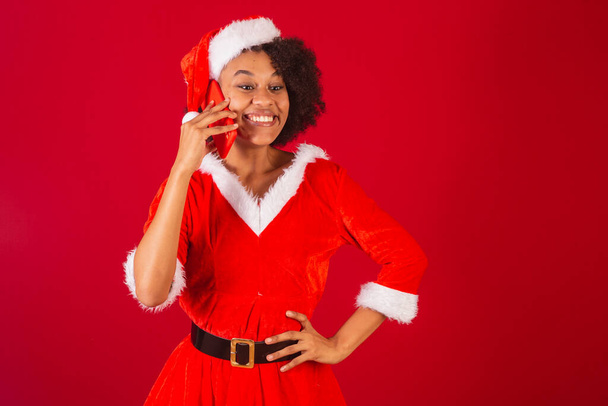 beautiful black brazilian woman, dressed as santa claus, mama claus, talking on voice call by smartphone, surprised, wow, amazing - Fotografie, Obrázek