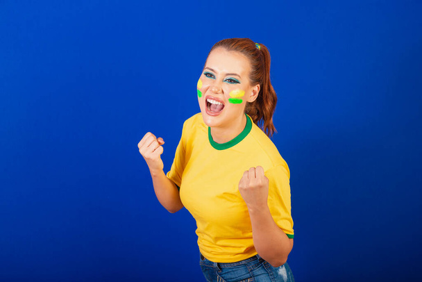 Caucasian woman, redhead, Brazil soccer fan, Brazilian, blue background, screaming goal - Valokuva, kuva