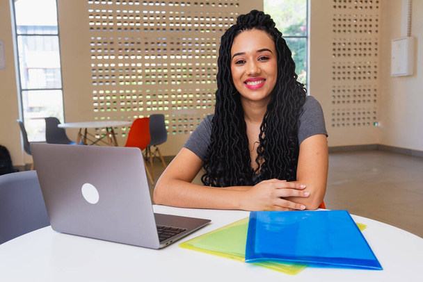 giovane donna di colore, brasiliana, studente universitario che lavora su notebook, sorridente alla macchina fotografica. - Foto, immagini