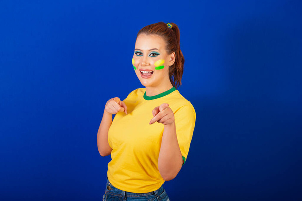 Caucasian woman, redhead, Brazilian soccer fan, Brazilian, blue background, pointing at camera, choosing you. - Fotografie, Obrázek