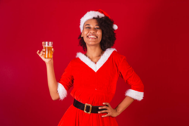 beautiful black brazilian woman, dressed as santa claus, mama claus, holding glass of beer - Foto, imagen