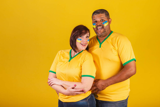 Couple, red-haired woman and black man, Brazilian soccer fans. Arms crossed, smiling at the camera. - Zdjęcie, obraz