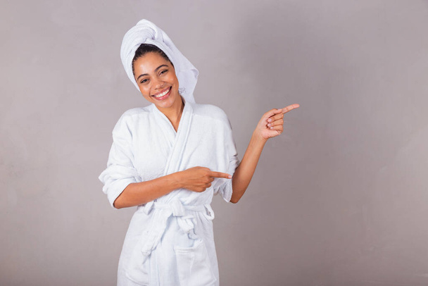 beautiful Brazilian black woman, wearing bathrobe and towel. pointing with fingers, showing right, spa, aesthetics, delicacy. - Fotografie, Obrázek