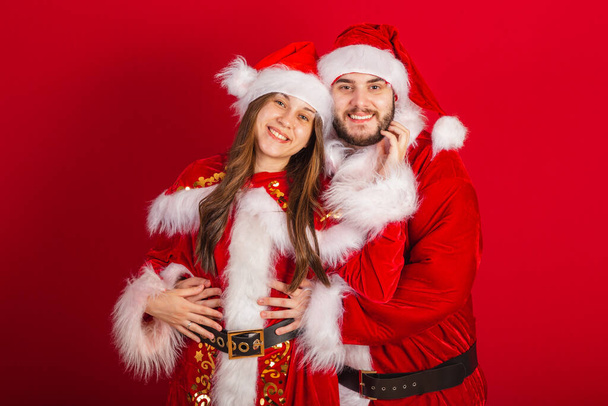 brazilian couple with christmas clothes, santa claus. romantically embraced. - Фото, изображение