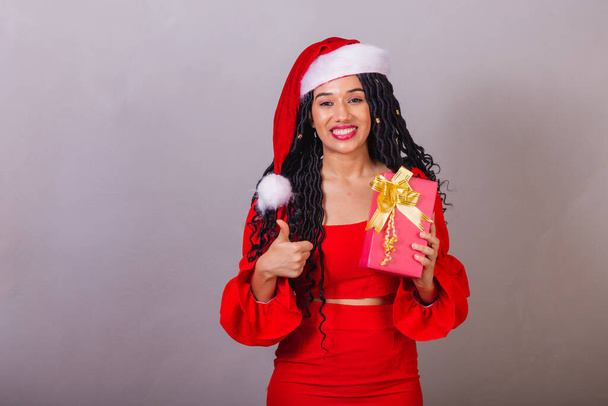 brazilian black woman, wearing christmas clothes, merry christmas, smiling, holding present. - Foto, Imagem
