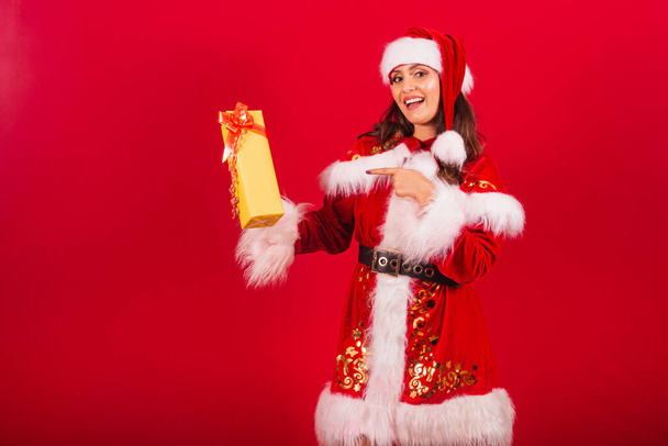 Brazilian woman dressed in Christmas clothes, Santa Claus. showing a yellow gift. - Foto, afbeelding