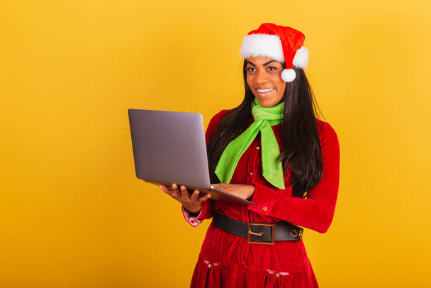 Beautiful black Brazilian woman, dressed in Christmas clothes, Santa Claus, holding notebook. - Foto, Bild