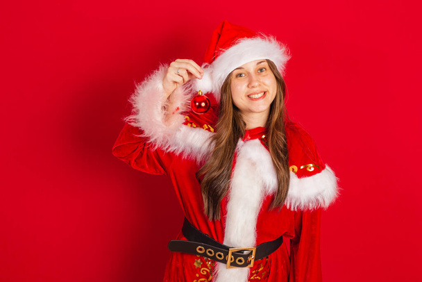 Caucasian, Brazilian woman in Christmas clothes, Santa Claus. Holding christmas ball. - 写真・画像