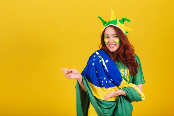 Caucasian, red-haired woman, soccer fan from Brazil, presenting products with her hands. - Foto, Bild