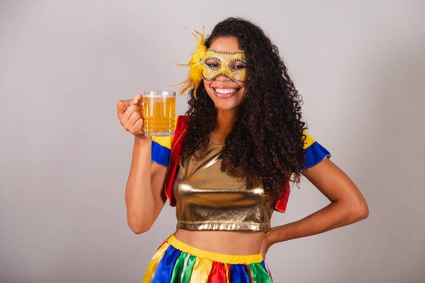 Bella donna brasiliana nera, con abiti da frevo, carnevale. in mascara, contenente un bicchiere di birra, festa in bar. - Foto, immagini