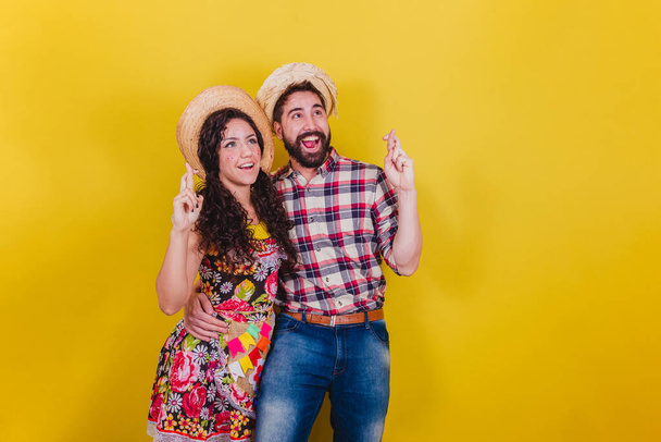 Beautiful couple dressed in typical clothes for a Festa Junina. Arraia de Sao Joao. Fingers crossed, cheering, wishing, luck concept. - Fotoğraf, Görsel