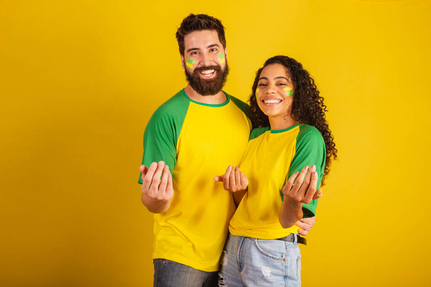 couple of brazil soccer supporters, dressed in the colors of the nation, black woman, caucasian man. inviting with hands. - Foto, immagini