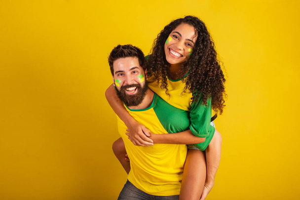 couple of brazil soccer supporters, dressed in the colors of the nation, black woman, caucasian man. kissing, love. - Foto, Imagem