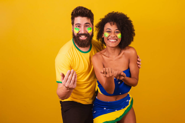 couple of brazilian soccer fans, dressed in the colors of brazil, black woman, caucasian man. inviting hands. calling, welcome - Valokuva, kuva