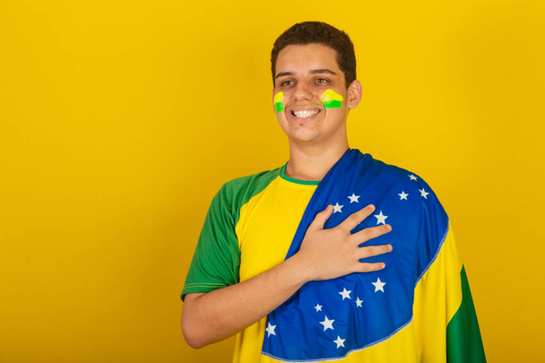 Young Brazilian man soccer fan. dressed in green, hand on chest, gratitude, national anthem. - Zdjęcie, obraz