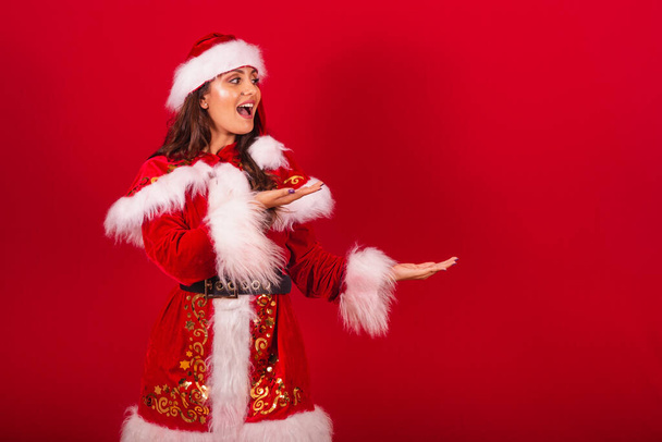 Brazilian woman dressed in Christmas clothes, Santa Claus. showing something to the right. - Foto, immagini
