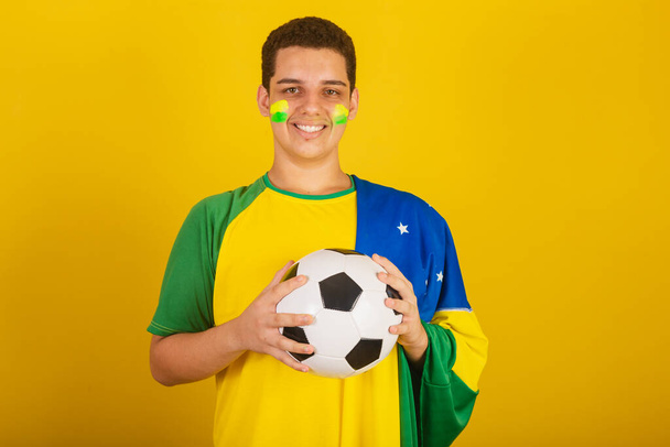 Young Brazilian man soccer fan. dressed in green, holding soccer ball with brazil flag. - Фото, зображення