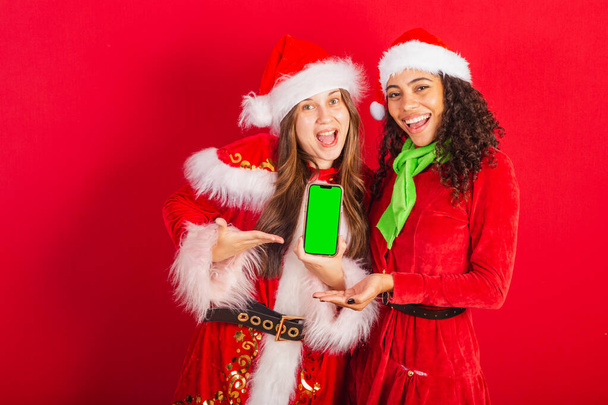 ブラジルの女性の友人、クリスマス服、サンタクロースと。スマートフォンの画面をクロマで表示. - 写真・画像