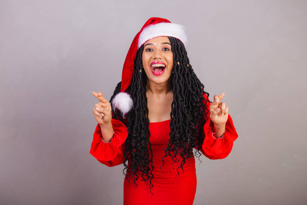 brazilian black woman wearing christmas clothes, merry christmas, smiling, fingers crossed cheering, wishing, sign of luck. - Foto, immagini