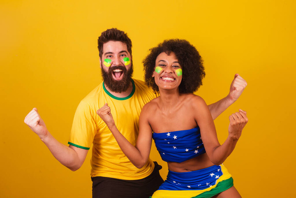 Pari brasilialaista jalkapallofania pukeutuneena brasilialaisen, mustan naisen, valkoihoisen miehen väreihin. Juhlimme, toivotamme tiimille onnea - Valokuva, kuva