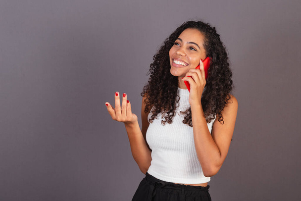 Young brazilian black woman talking on voice call, with red cell phone. - Photo, Image