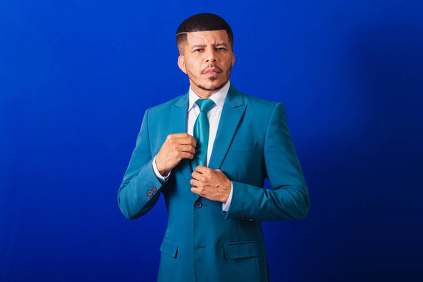 Brazilian black man, dressed in a suit and blue tie. business man. fixing tie - Photo, Image