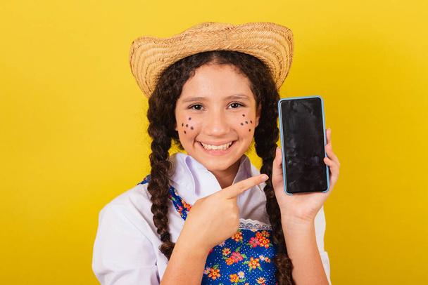 Girl wearing typical clothes for Festa Junina. pointing to mobile, apps, technology. For the Arraia party - Valokuva, kuva