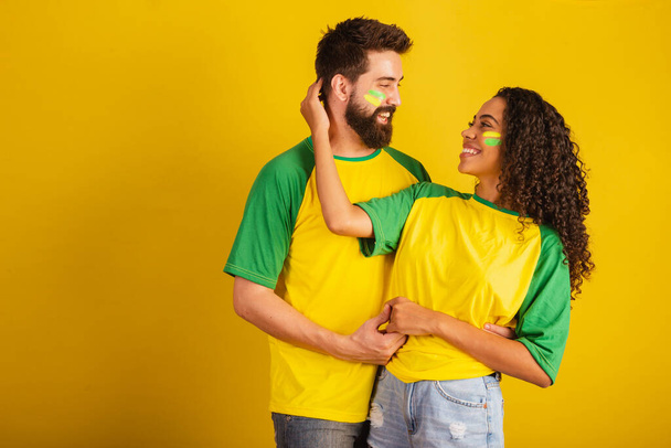 couple of brazil soccer supporters, dressed in the colors of the nation, black woman, caucasian man. embraced. - Photo, Image