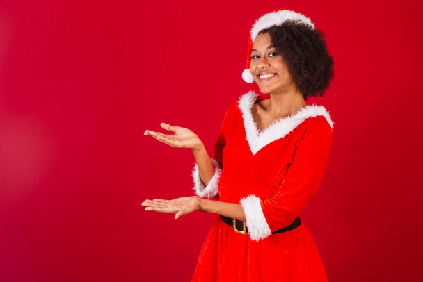 beautiful black brazilian woman, dressed as santa claus, mama claus, presenting product or information on the side - Foto, Imagem