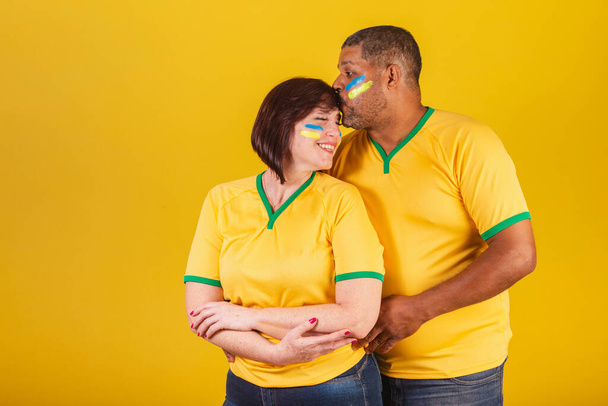 Couple, red-haired woman and black man, Brazilian soccer fans. Arms crossed, smiling at the camera. - Valokuva, kuva