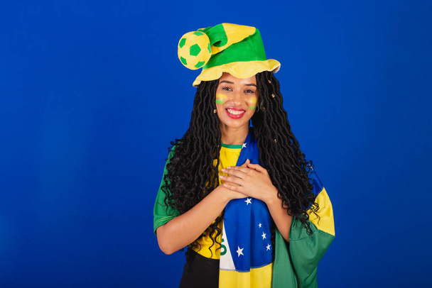 Young black Brazilian woman, soccer fan. with brazil flag. with hand on chest, gratitude. - Fotografie, Obrázek