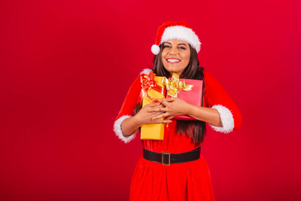 beautiful Brazilian woman dressed in Christmas clothes, Santa Claus. hugging two gifts. - 写真・画像