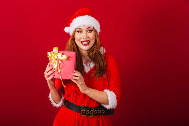 beautiful Brazilian red-haired woman, dressed in Christmas clothes, Santa Claus. holding red gift. - Фото, зображення