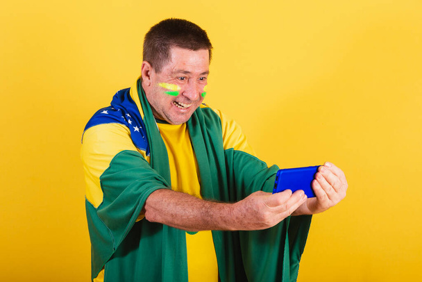 adult man, brazil soccer fan, using flag, smartphone, watching game by cellphone. online, streaming - Фото, зображення