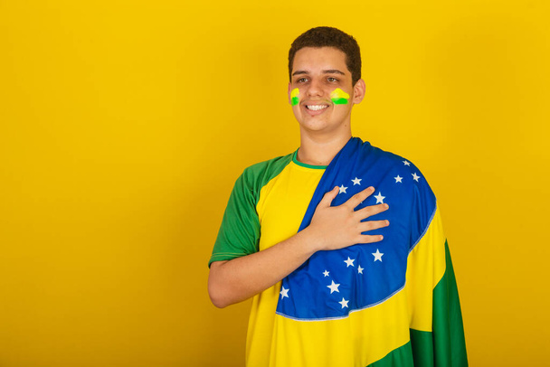 Young Brazilian man soccer fan. dressed in green, hand on chest, gratitude, national anthem. - 写真・画像