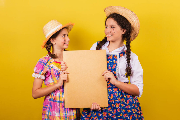 sisters and friends, wearing typical clothes of the Festa Junina. Holding sign for text or advertisement. - Zdjęcie, obraz