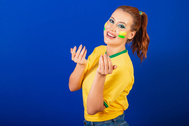 Caucasian woman, redhead, Brazil soccer fan, Brazilian, blue background, inviting with hands, calling - Foto, afbeelding