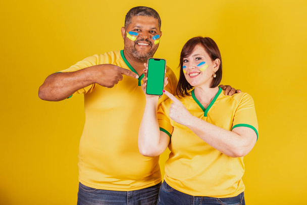 Casal, ruiva e negro, fãs de futebol brasileiro. Smartphone, celular online. - Foto, Imagem