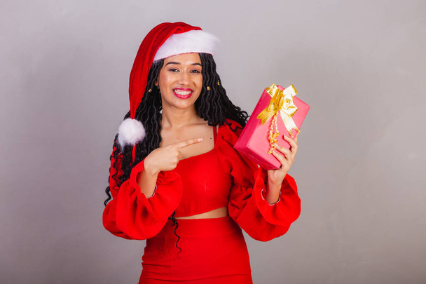 brazilian black woman, wearing christmas clothes, merry christmas, smiling, holding present. - Foto, immagini