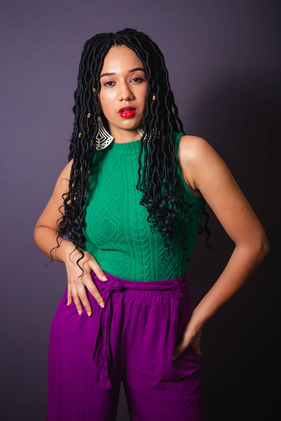 Beautiful Brazilian black woman, dressed in green and purple. Half body portrait, gray infinity background. - 写真・画像