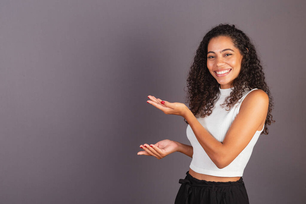 Young Brazilian black woman presenting with her hands to the left, publicity photo. - Foto, Bild