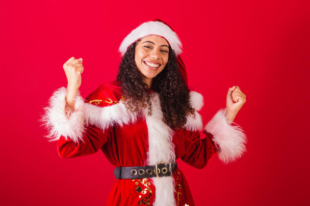 beautiful brazilian black woman, dressed as santa claus, christmas clothes. celebrating, vibrating in happiness. - Фото, изображение