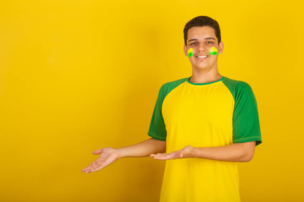 Joven aficionado al fútbol brasileño. vestido de verde, presentando algo - Foto, Imagen