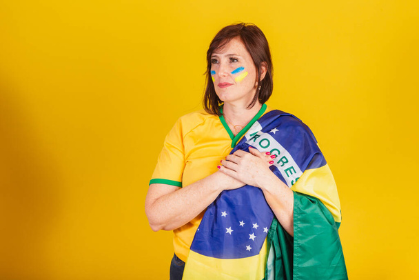 red-haired woman, Brazilian soccer fan. with his hands on his chest singing the national anthem. Democracy. - Zdjęcie, obraz